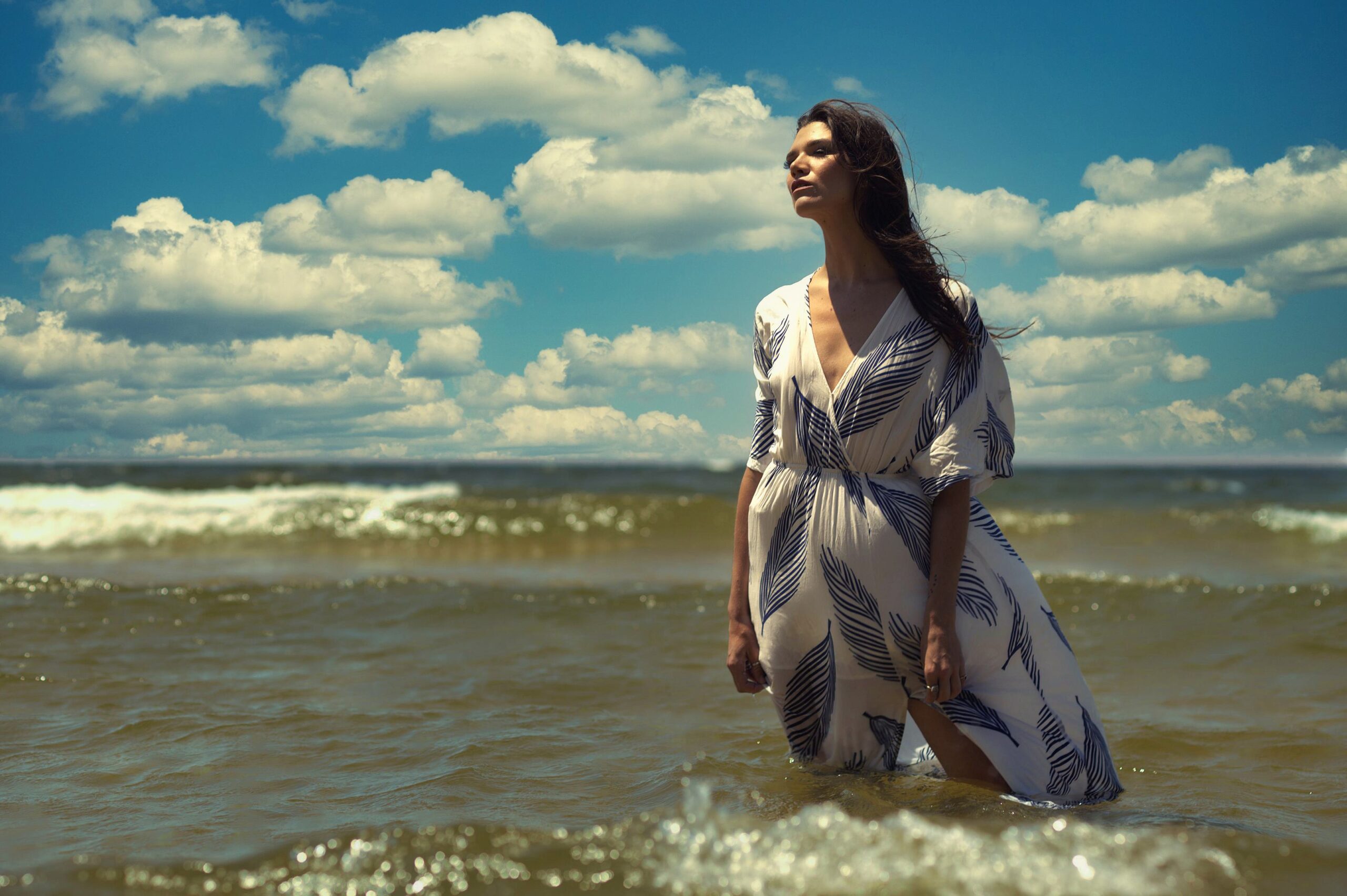 Fashion portrait of a woman standing in Lake Michigan waves wearing a white and blue leaf print maxi dress, west Michigan shoreline photography