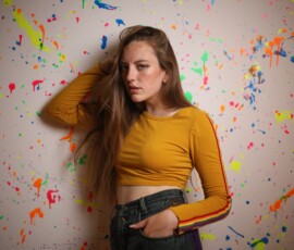 Grand Rapids Michigan Indoor Fashion Photography — Paint Splatter Wall Fashion portrait of woman in mustard yellow crop top leaning against colorful paint splatter wall at indoor studio Grand Rapids Michigan