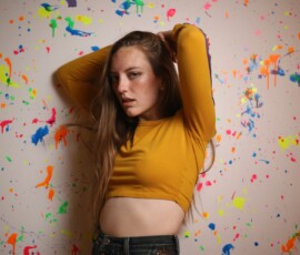 Creative Indoor Fashion Portrait — Grand Rapids Michigan Fashion portrait of woman in mustard yellow crop top hands in hair against colorful paint splatter wall indoor studio Grand Rapids Michigan