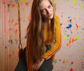 Indoor Swing Fashion Portrait — Grand Rapids Michigan Paint Wall Fashion portrait of woman in mustard yellow crop top leaning forward on yellow chain swing against paint splatter wall indoor studio Grand Rapids Michigan