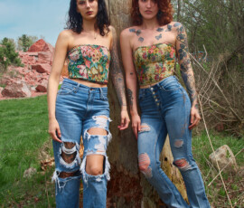 Detroit Metro Michigan Editorial Outdoor Fashion Photography — Duo Floral Corset Distressed Denim Dead Tree Green Grass editorial outdoor fashion portrait two tattooed models standing weathered dead tree dark hair glasses jewel-toned floral corset wide-leg distressed jeans auburn hair yellow floral corset high-waist button-front flare jeans green spring grass red rock quarry Detroit Metro Michigan
