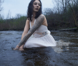 Moody Outdoor Fashion Photography Detroit Metro Michigan — White Dress River Session Moody outdoor fashion portrait woman soaking white boho dress rose tattoo sleeve crouching river downward gaze Detroit Metro Michigan