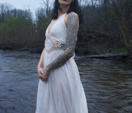Detroit Metro Michigan Ethereal Outdoor Fashion Photography — White Dress River Ethereal outdoor fashion portrait woman white boho maxi dress rose tattoo sleeve standing river hands clasped overcast sky Detroit Metro Michigan
