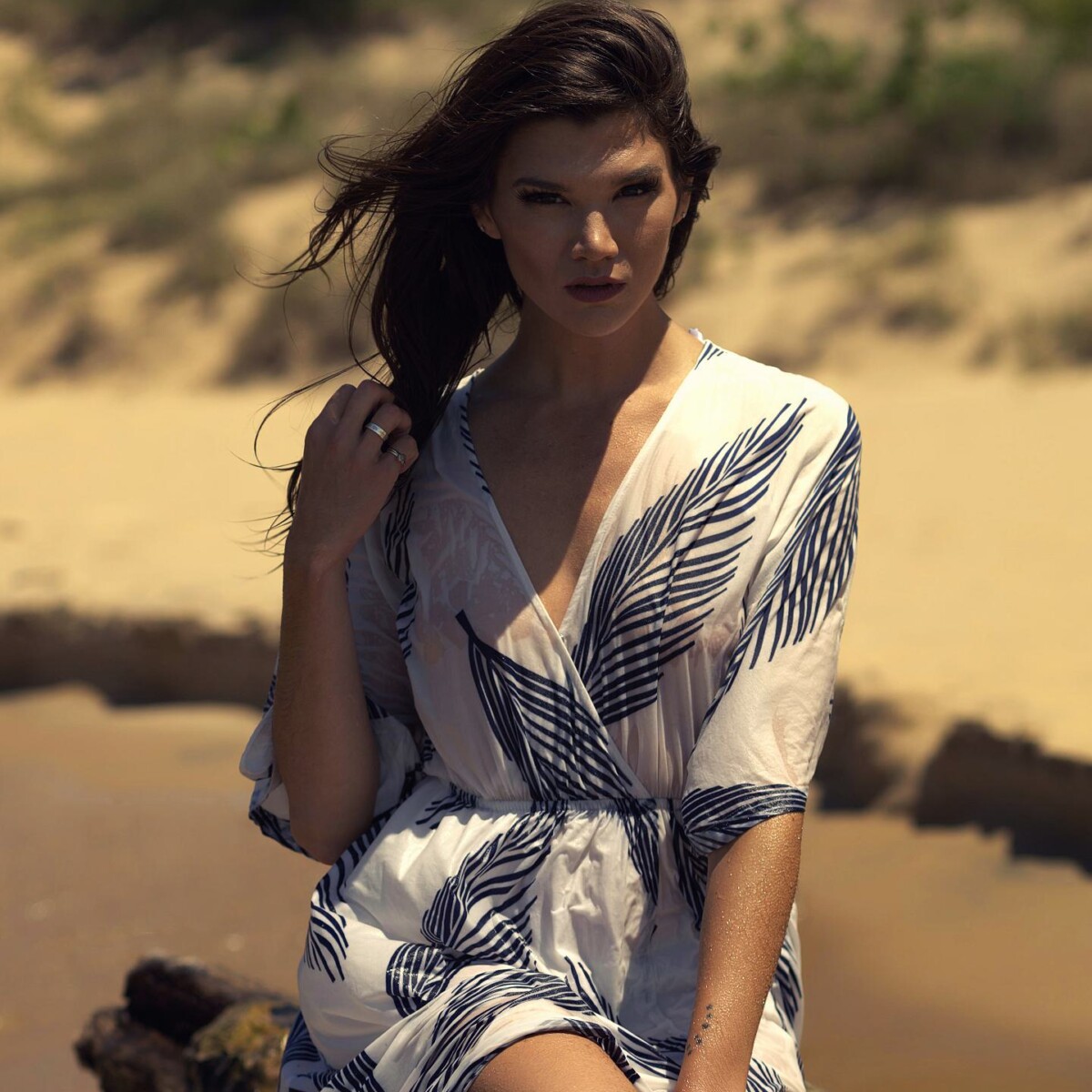 Lake Michigan Beach Portrait — West Michigan Fashion portrait session on Lake Michigan beach, woman in white and blue printed dress seated on rocks with sandy shore and trees in background, west Michigan photographer