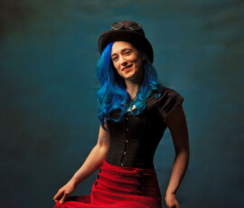 Metro Detroit Steampunk Creative Fashion Photography — Oakland County Michigan Joyful steampunk concept fashion portrait of woman with blue hair in black corset red ruffled skirt smiling holding skirt Oakland County Michigan
