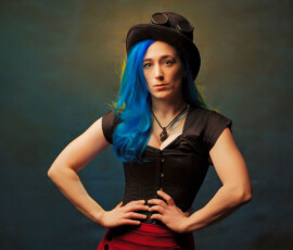 Powerful Steampunk Studio Portrait — Oakland County Michigan Powerful steampunk concept fashion portrait of woman with blue hair black corset red skirt hands on hips direct gaze Oakland County Michigan