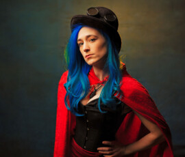 Dramatic Red Cape Steampunk Fashion Portrait — Oakland County Michigan Dramatic steampunk concept fashion portrait of woman with blue hair in black corset red cape and top hat with goggles Oakland County Michigan