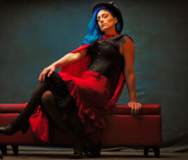 Moody Steampunk Studio Portrait on Red Ottoman — Oakland County Michigan Moody steampunk concept fashion portrait of woman with blue hair red cape seated on red ottoman eyes closed Oakland County Michigan