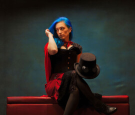 Creative Steampunk Studio Fashion Portrait — Oakland County Michigan Photographer Creative steampunk concept fashion portrait of woman with blue hair hand in hair holding steampunk top hat seated on red ottoman Oakland County Michigan