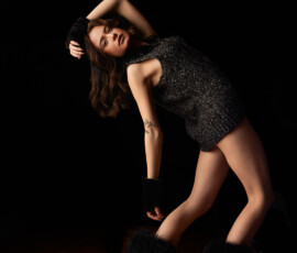 Detroit Metro Michigan Avant-Garde Dark Studio Fashion Photography — Charcoal Boucle Dress Deep Body Arch Avant-garde dark studio fashion portrait woman charcoal boucle zip dress fingerless gloves shaggy boots dramatic forward arch hand on headband upward gaze hair loose botanical tattoo warm floor Detroit Metro Michigan