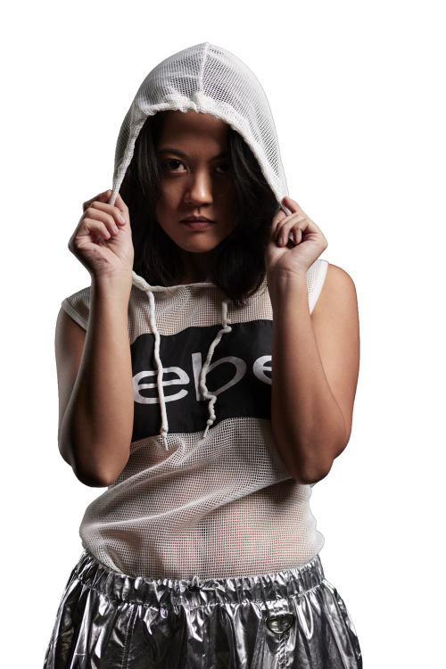 Fashion portrait of a model in a white mesh hooded top and metallic pants, lit with dramatic studio lighting against a black background, photographed in Metro Detroit